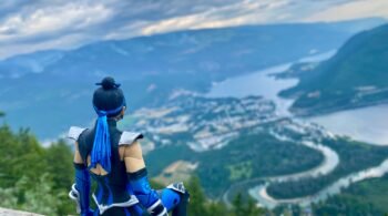 Figure of a warrior in blue armor sitting on a mountain ledge overlooking a scenic landscape.