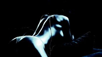 Sensual back view of a woman lying on a couch, showcasing the curves of her back in low, moody lighting.