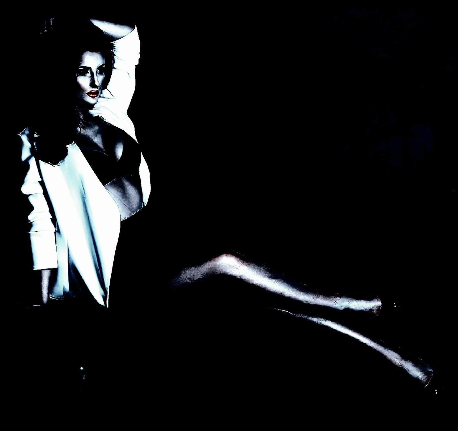 A woman in a black bra and white jacket, reclining seductively against a black backdrop.