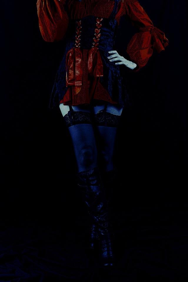 Vintage-inspired black corset outfit paired with lace stockings, shot in a moody, dark setting.