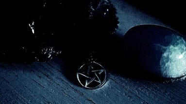 Close-up of a dark pentagram necklace resting on a wooden surface, surrounded by shadows in a gothic, eerie setting.