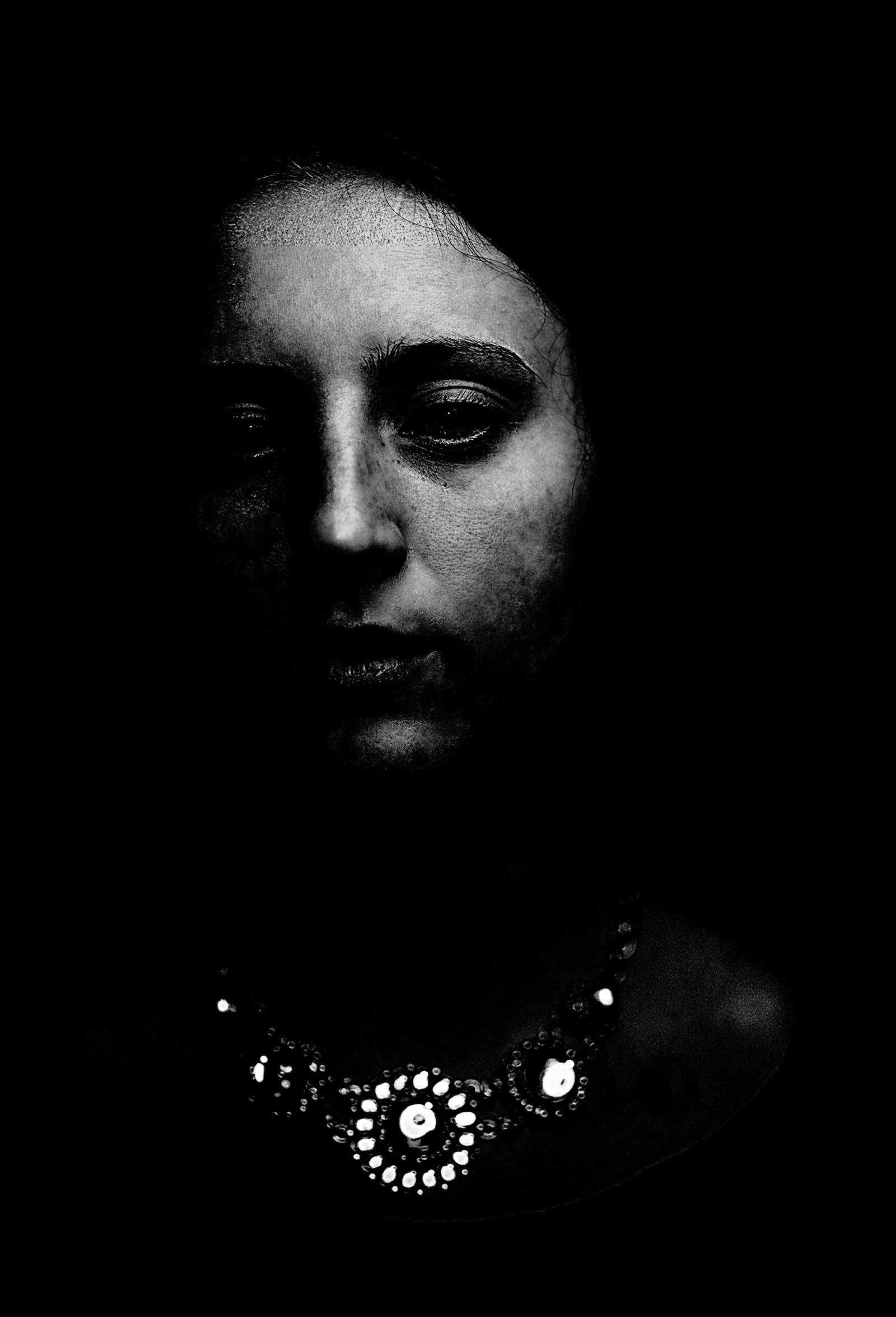 Moody portrait of a woman wearing an ornate gothic necklace, her face half-hidden in shadows, exuding a sense of melancholy.