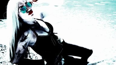 A tattooed woman lounging on the beach in edgy swimwear, wearing reflective aviator sunglasses and sporting bold red lips, blending metalhead style with a seaside vibe.