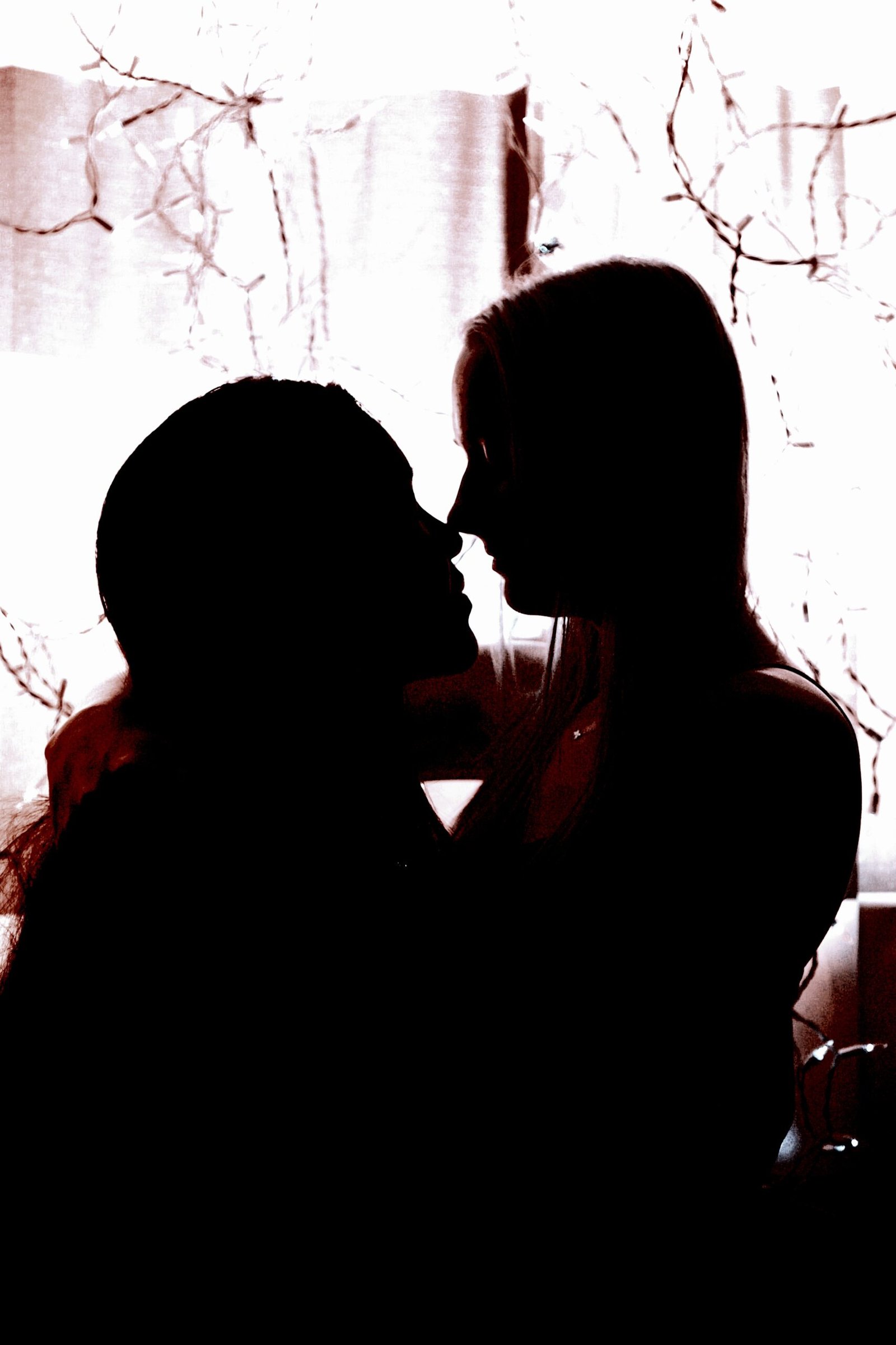 Silhouetted profile of two people close together, with delicate lights and a soft background, conveying affection and tenderness.