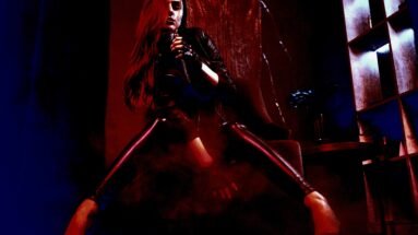Dark, sultry woman in black leather pants and heels sitting in a dramatic pose, enveloped in red lighting and smoke for a gothic aesthetic.