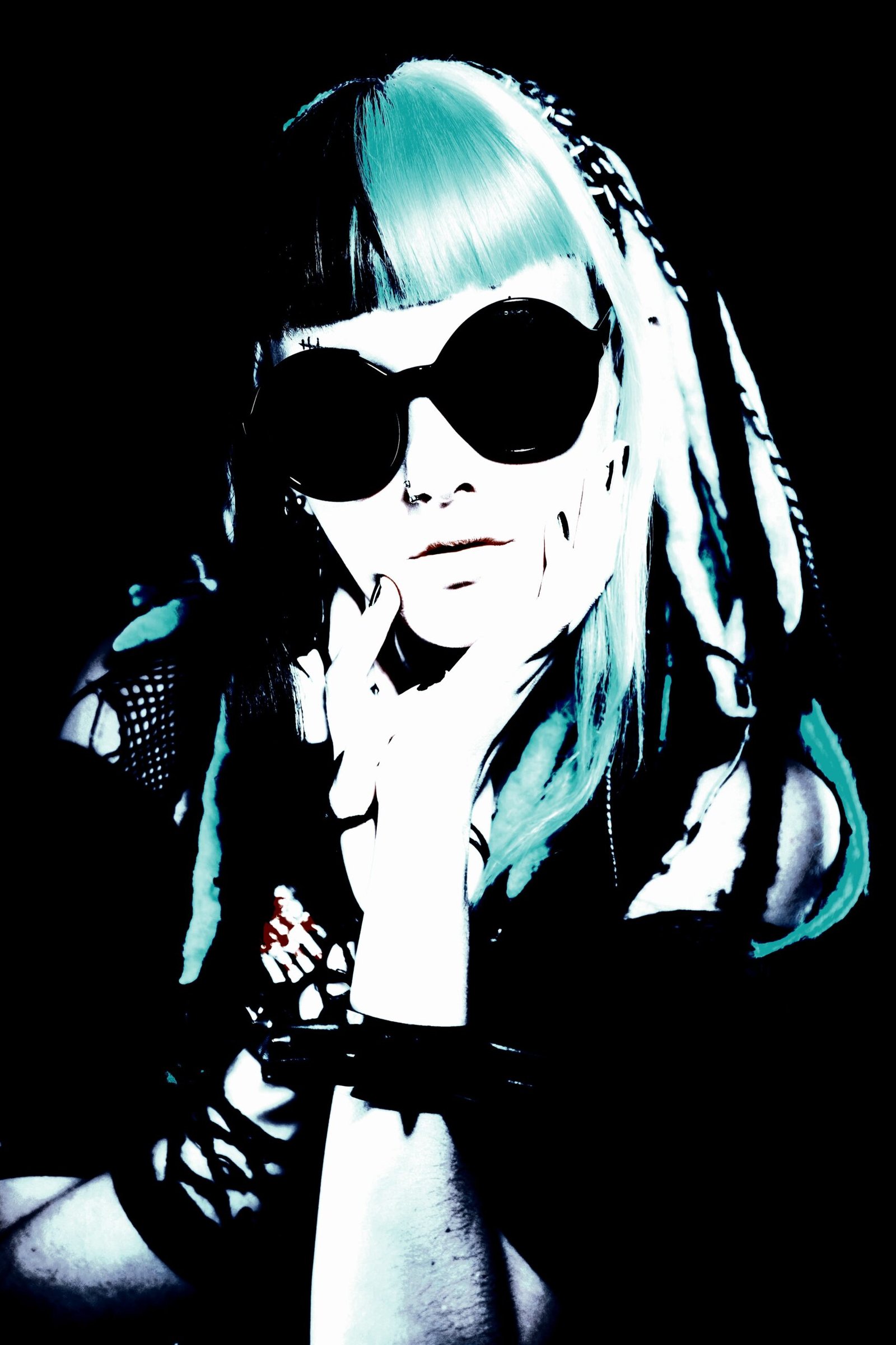 A striking woman with alternative hair and large, round sunglasses, staring intensely into the camera, creating a bold and edgy visual impact in a dark, moody setting.