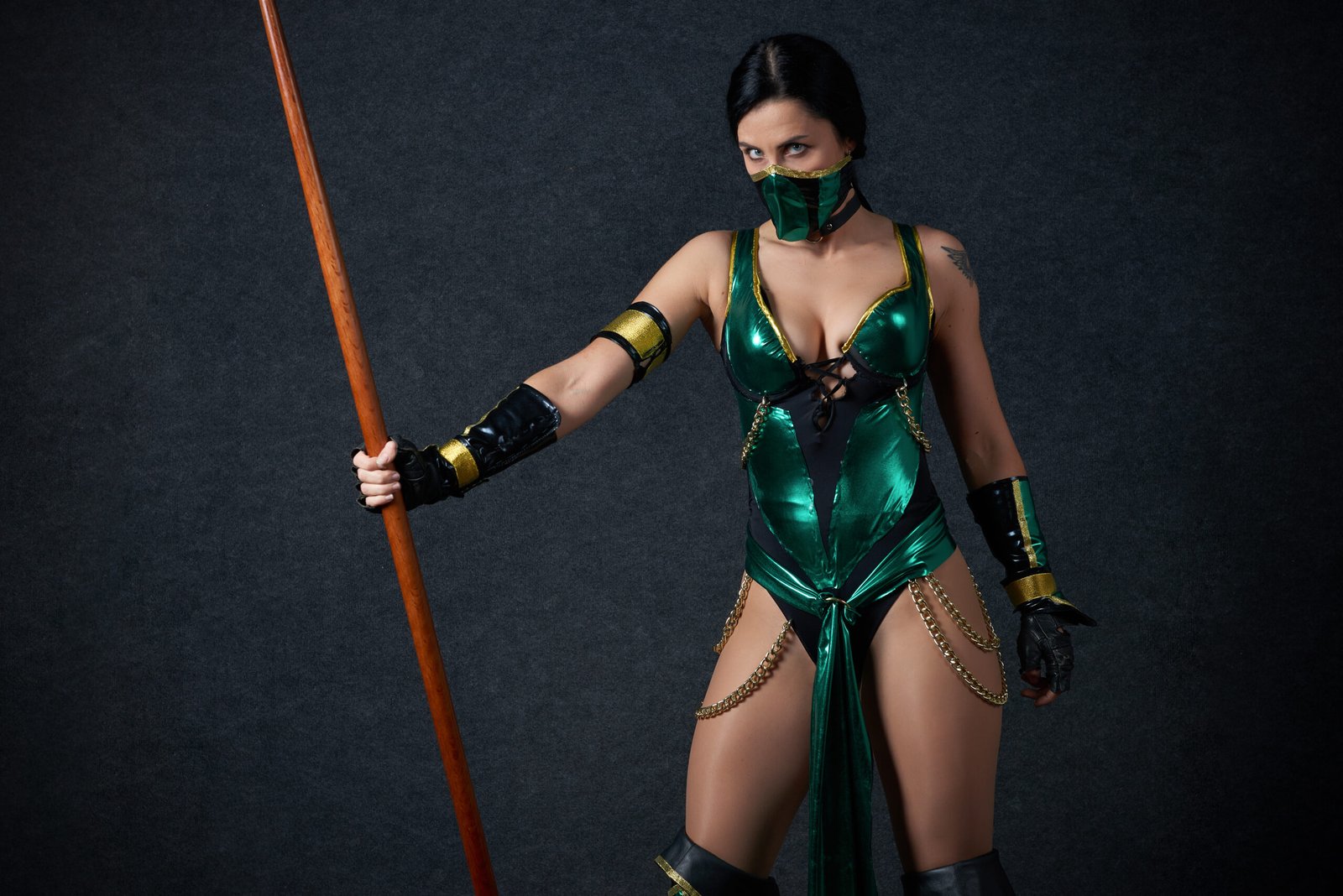 Female cosplayer dressed as Jade from Mortal Kombat, holding a staff and wearing a green outfit with golden accessories.