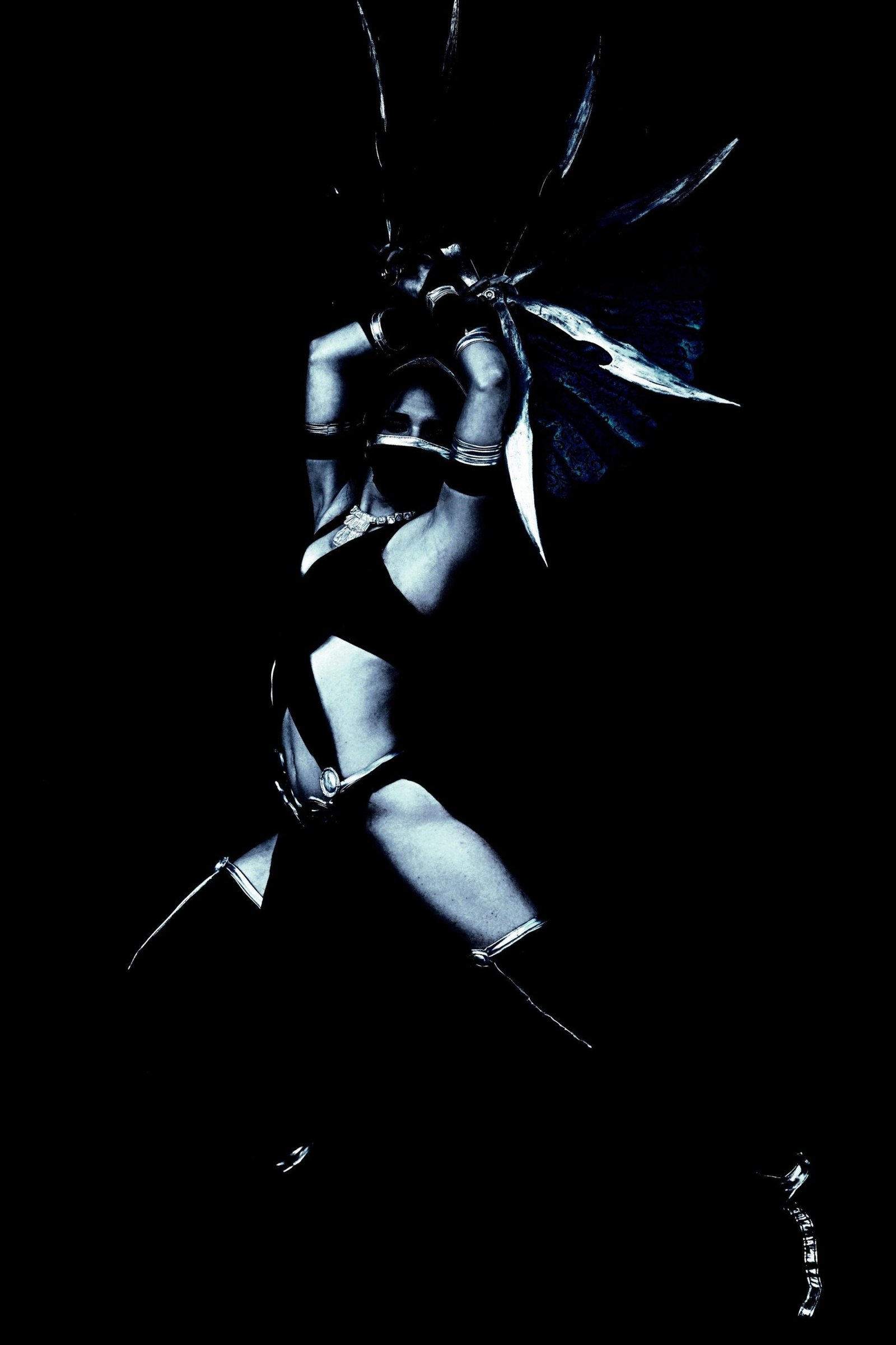 Alternative cosplay with a warrior character in an exotic and dramatic headdress, posed powerfully in a dark, shadowed setting.