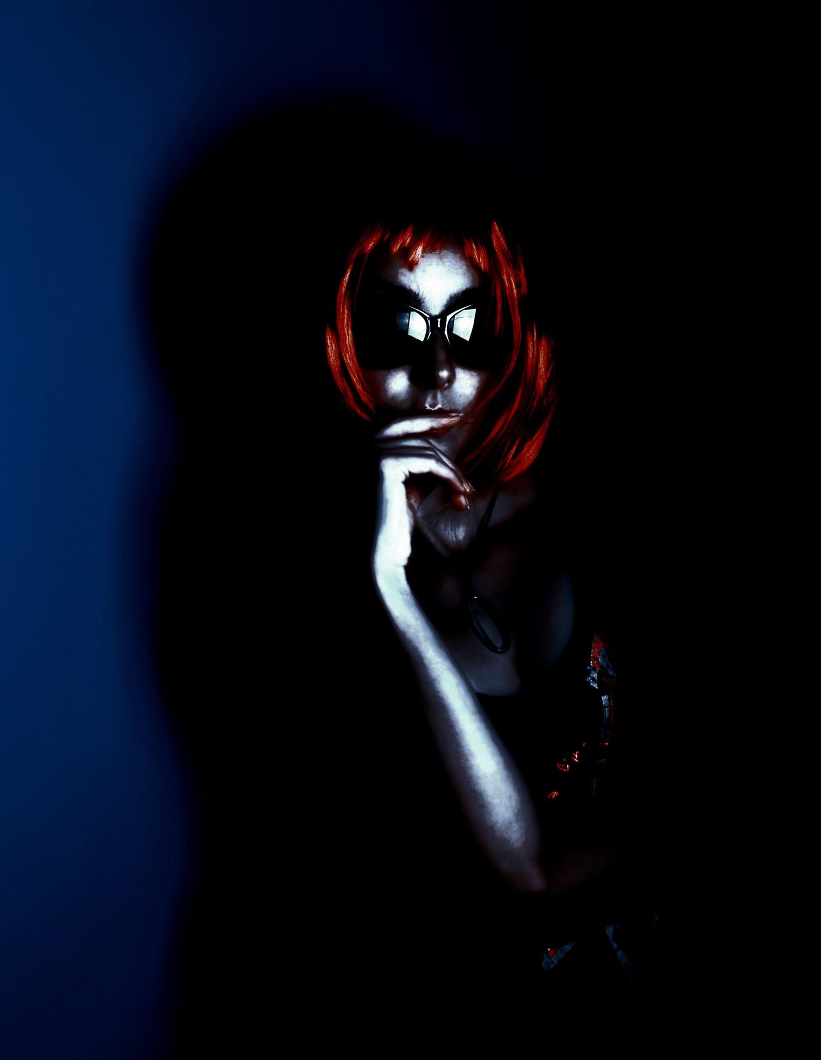 A woman with a sharp, fiery red bob, wearing black sunglasses, contemplating in the shadows with her hand resting on her chin, creating a mysterious, noir-like atmosphere.