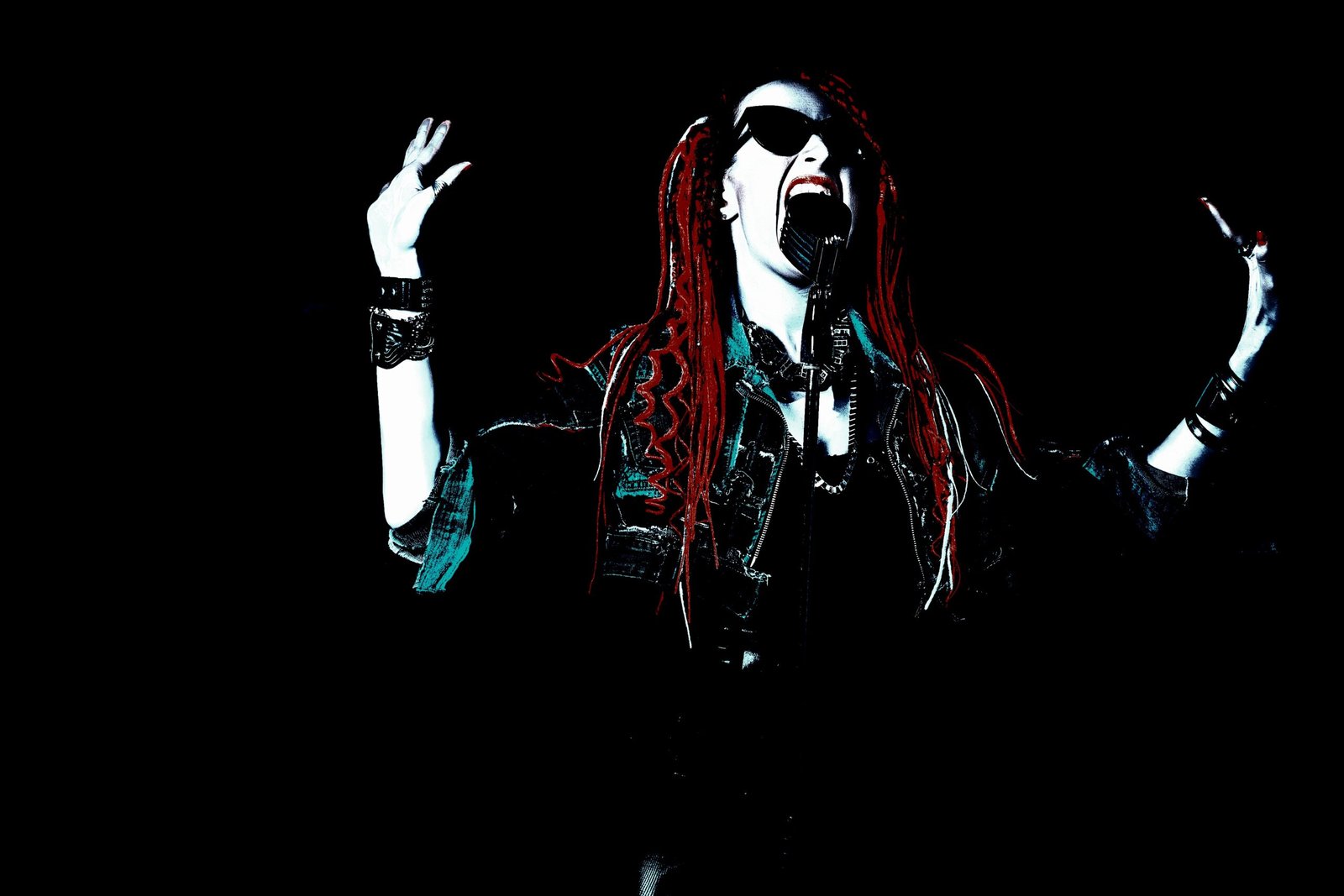 A female metal singer in mid-performance, wearing dark sunglasses and with fiery red dreadlocks, passionately belting out a song into a vintage microphone, radiating pure metal energy on stage.