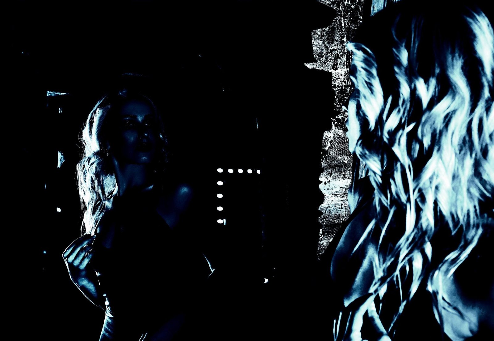 Blonde woman gazing into a mirror in a moody, dramatic light, emphasizing self-reflection and mystery.