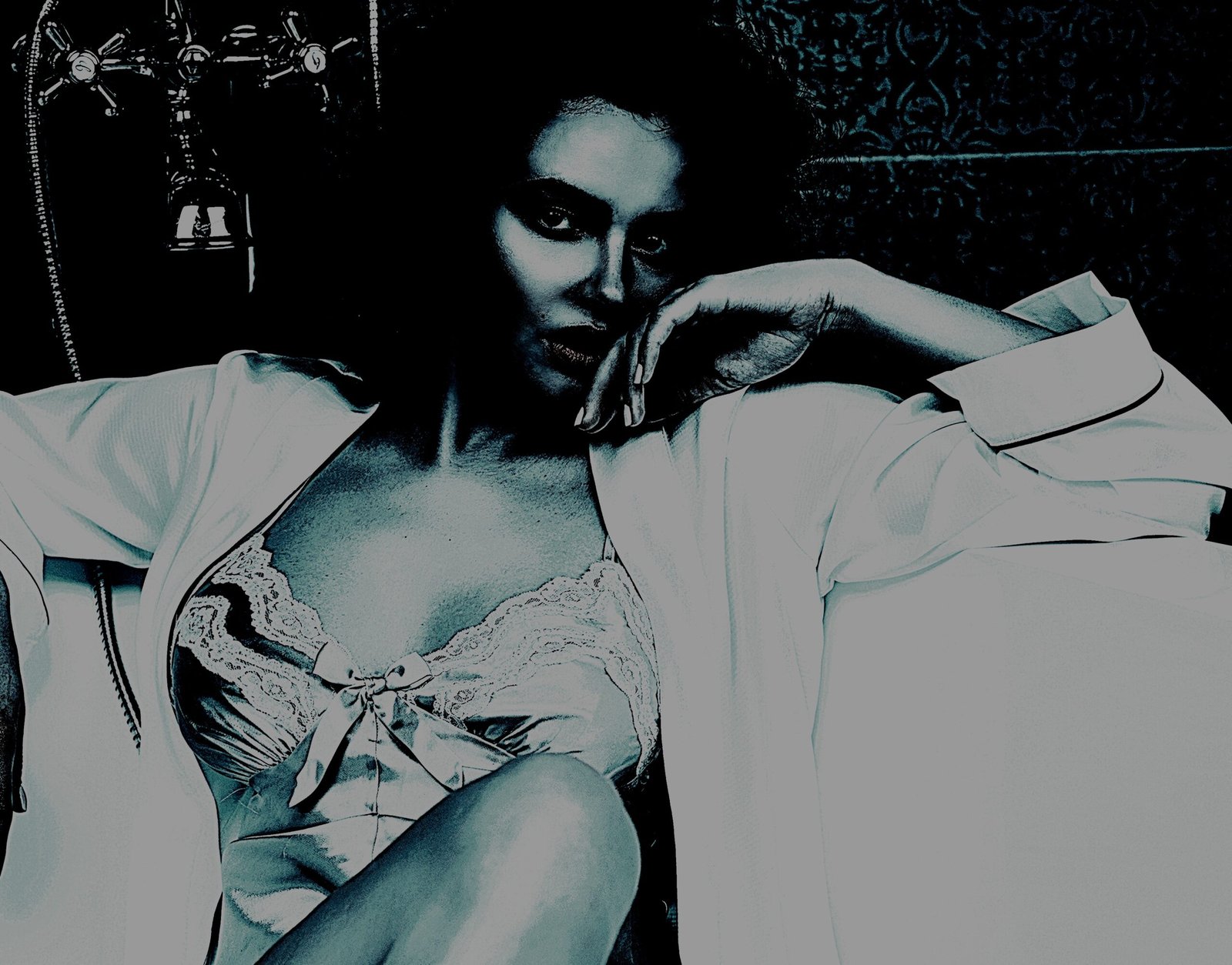 Woman in a satin and lace nightgown leaning against a bathtub, with a thoughtful and alluring expression in dim lighting.