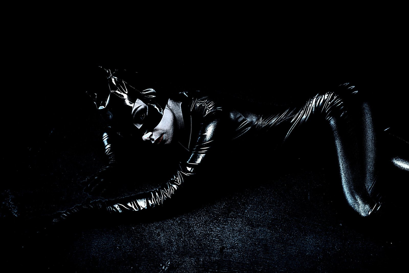 Sleek black latex catsuit cosplay of a femme fatale character, sprawled across a dark surface, exuding stealth and danger.