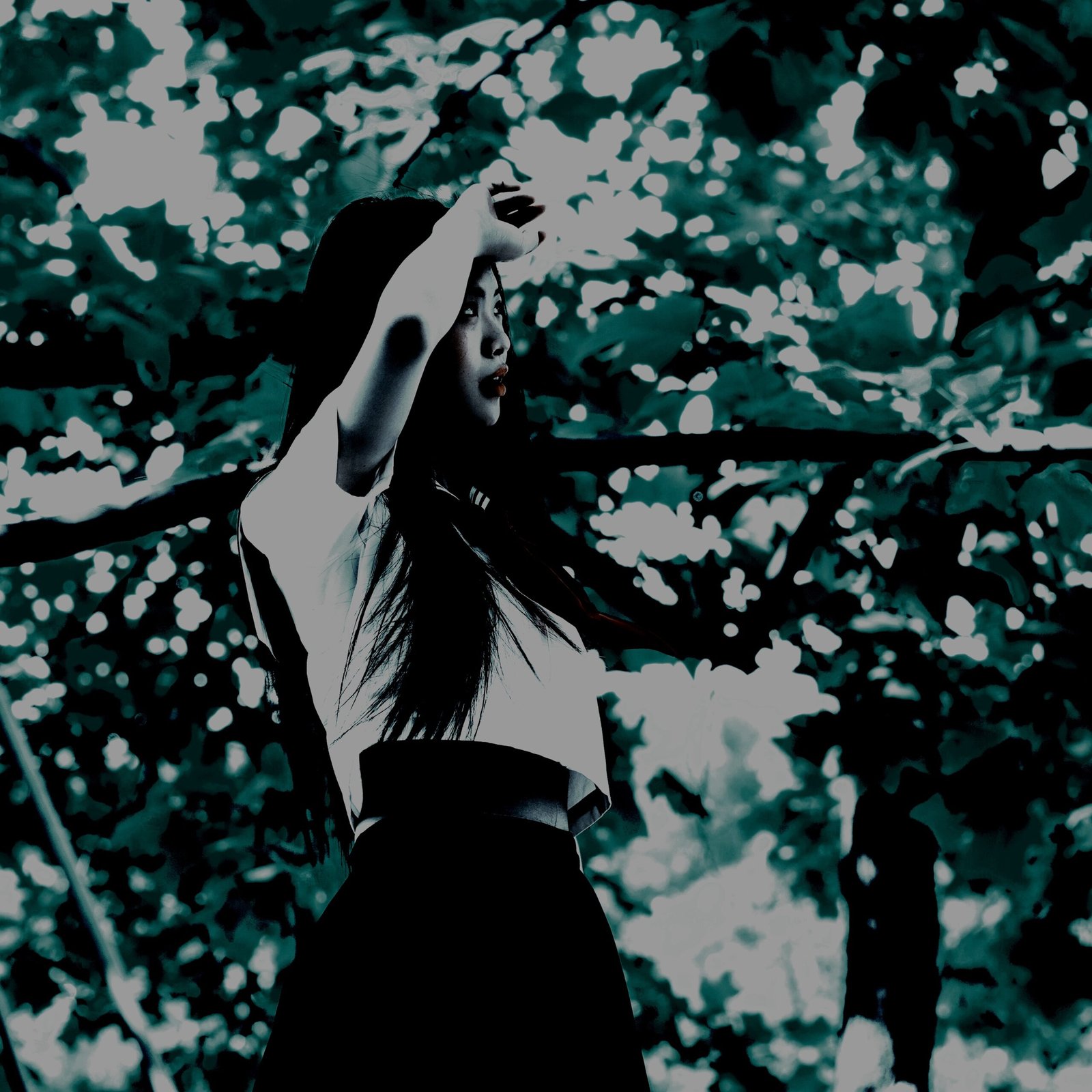 Dark and moody cosplay of a mysterious character in a white top and flowing black skirt, standing in a shadowy forest setting.