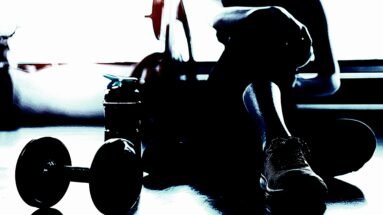 Silhouette of a person resting after a workout, with dumbbells and water bottle on the floor, capturing the calm after the intensity of exercise.