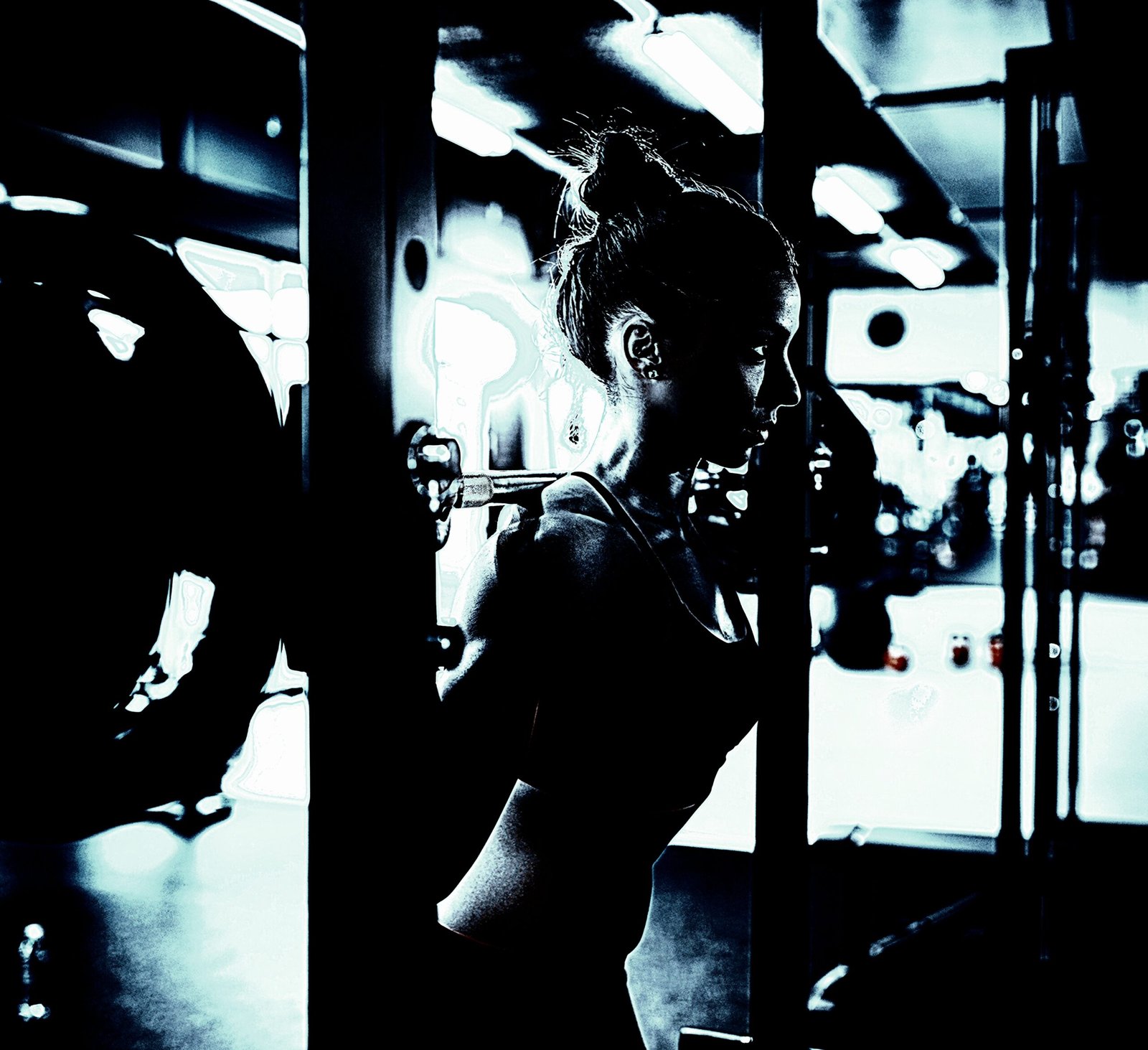 Woman lifting weights in a gym, demonstrating strength and focus during a barbell squat in a dimly lit setting.