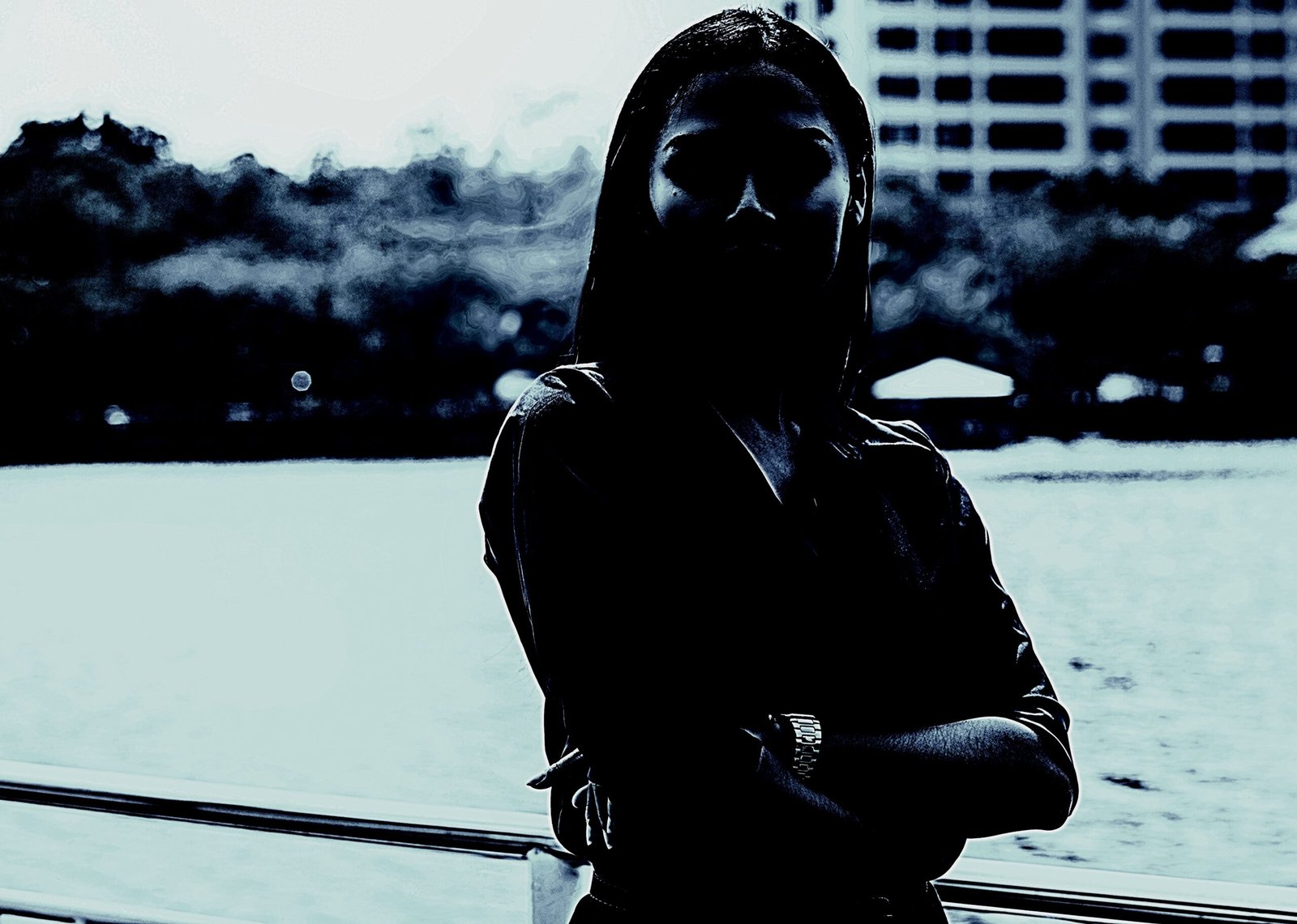 Silhouetted woman standing by a waterfront railing, with a dark cityscape in the background, conveying mystery and introspection.
