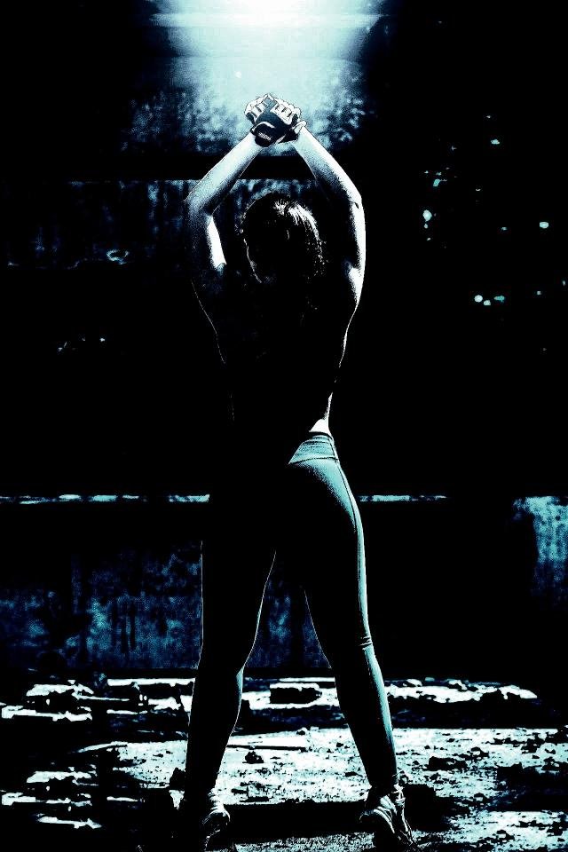 Back view of a woman stretching in a dimly lit industrial setting, highlighting strength and mobility.