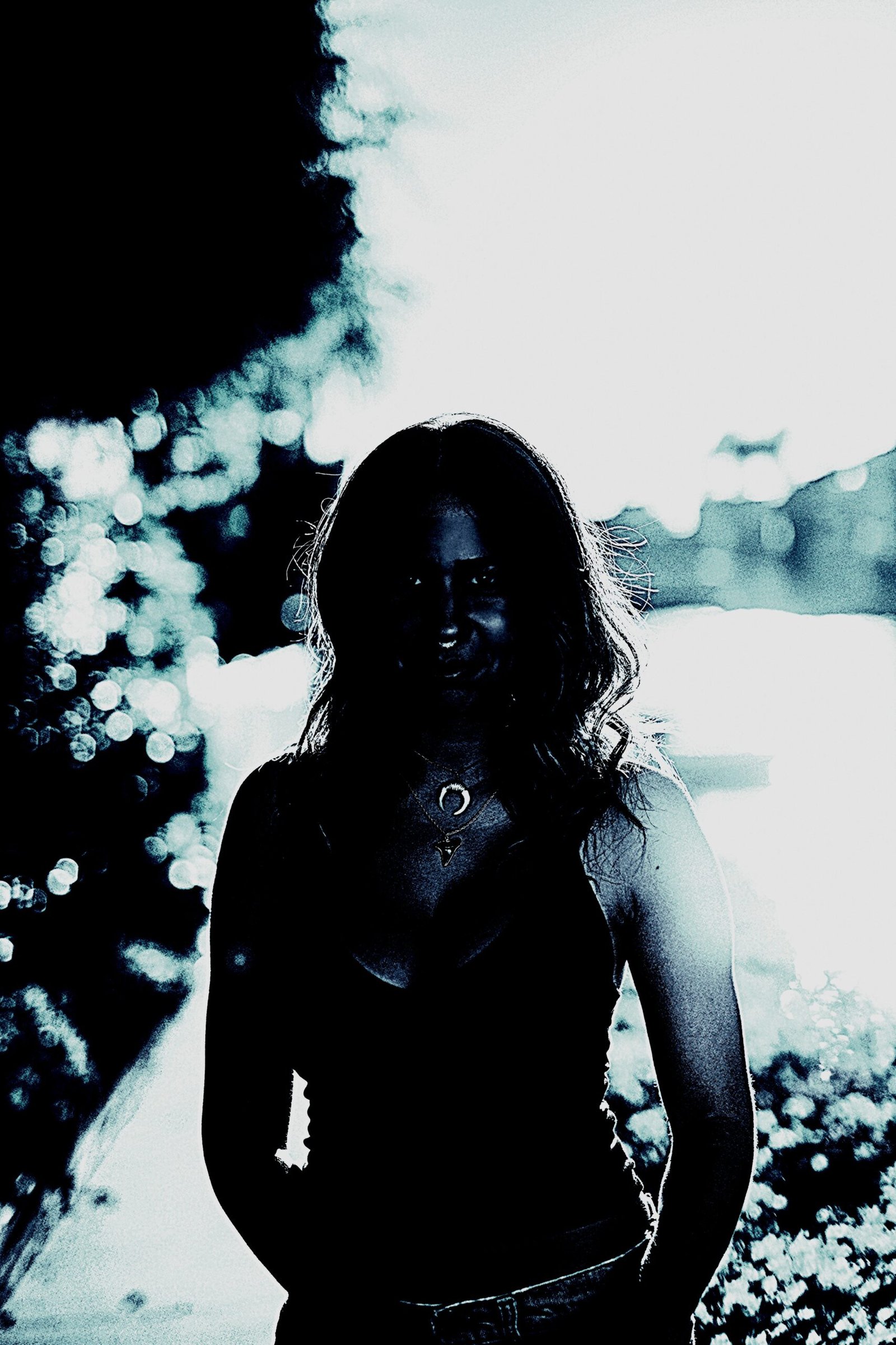 A mysterious silhouette of a woman standing outdoors, with light filtering through the background, creating an enigmatic and moody atmosphere.