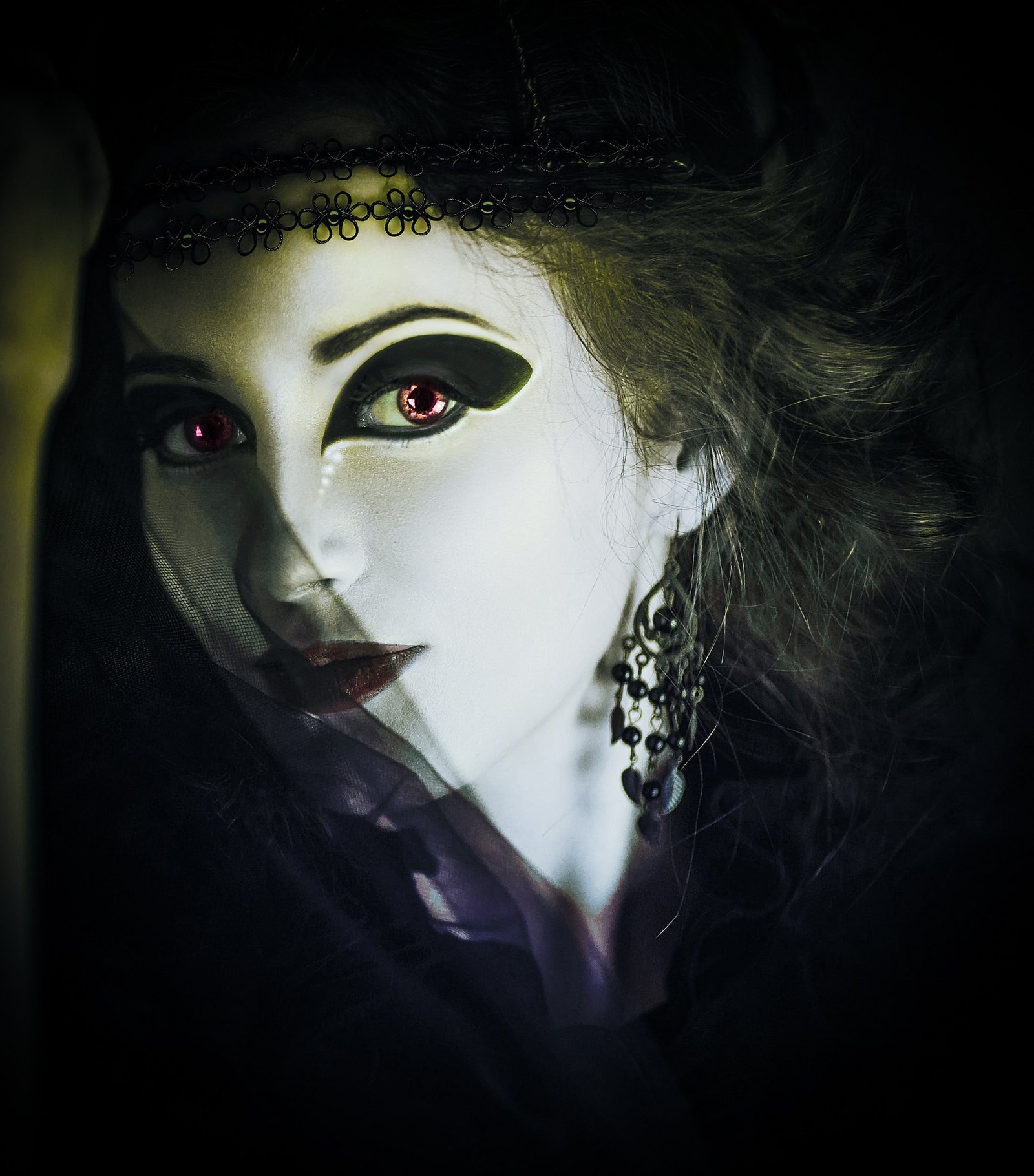 Close-up of a mysterious woman with vampire-inspired makeup and red glowing eyes, adorned with black lace accessories.