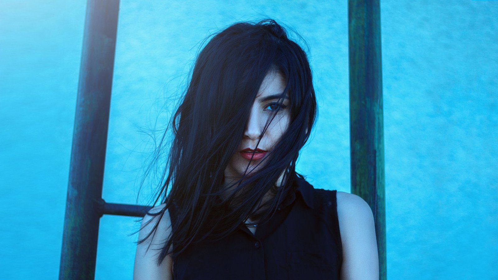 Shadowy figure of a gothic woman with long black hair and a haunting expression, bathed in eerie teal light.