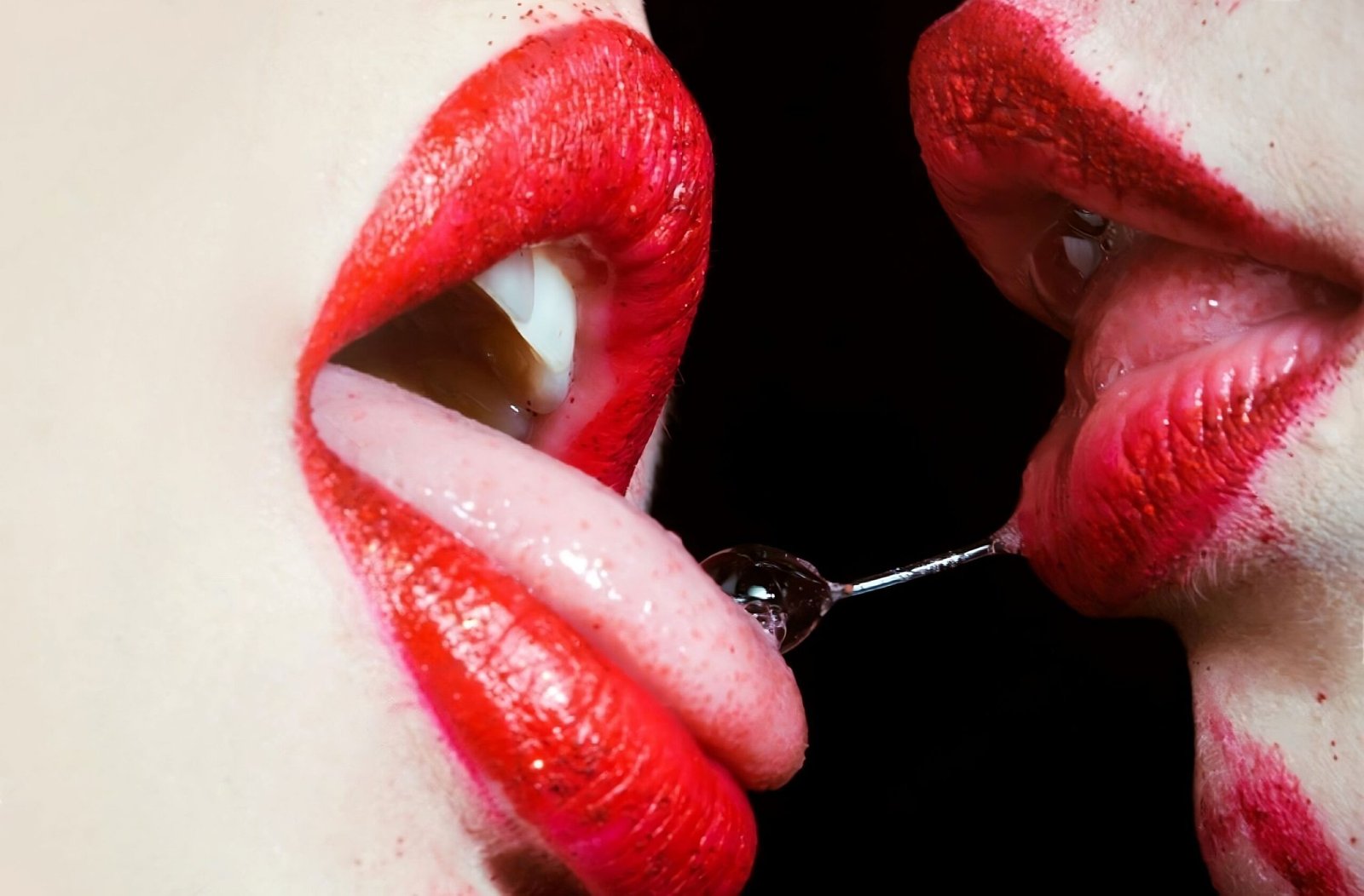 A close-up of two women engaging in a playful and provocative moment, emphasizing the allure of red lipstick.