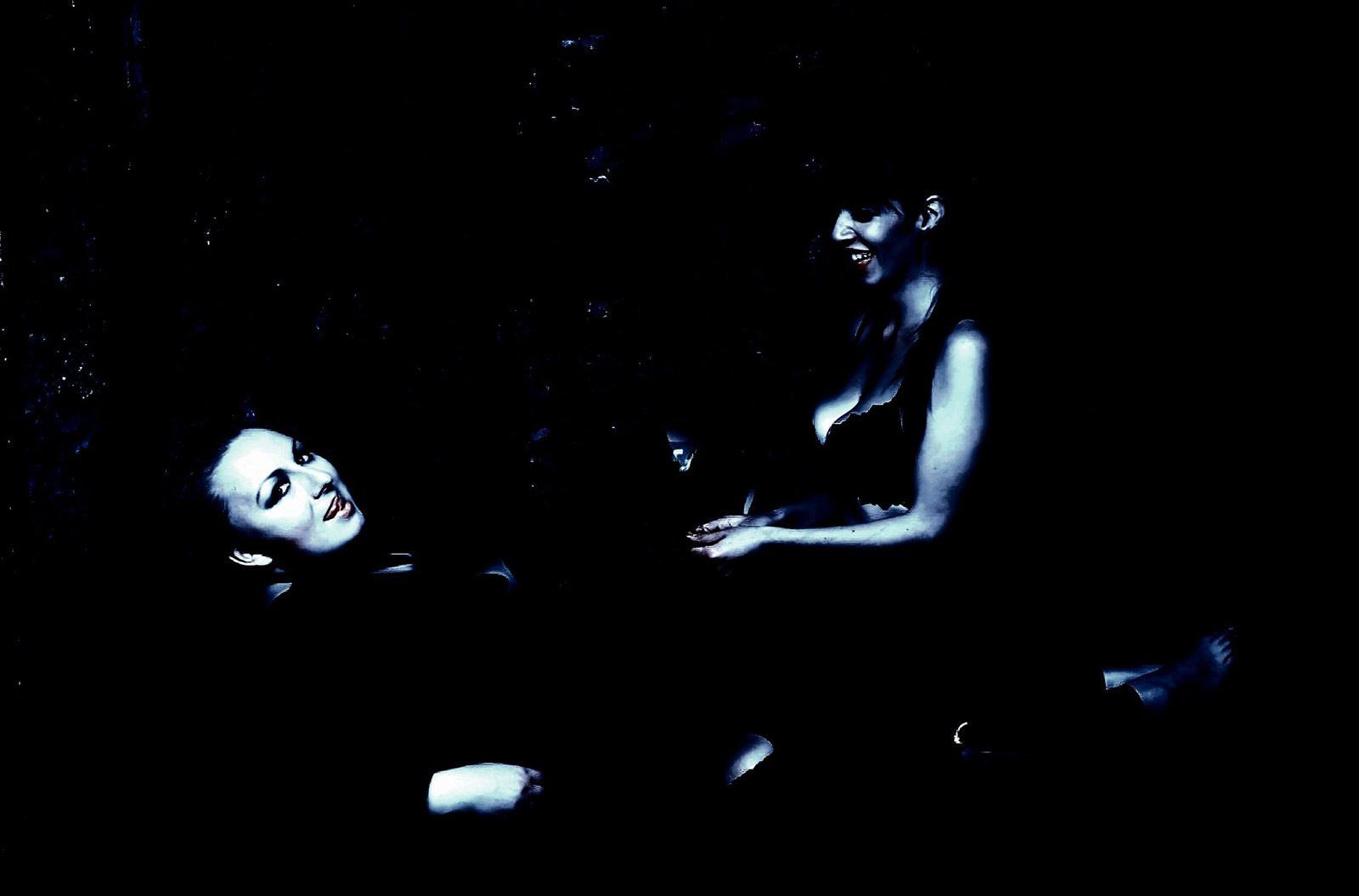 Two women in a dimly lit room, laughing together, creating an intimate, relaxed ambiance.