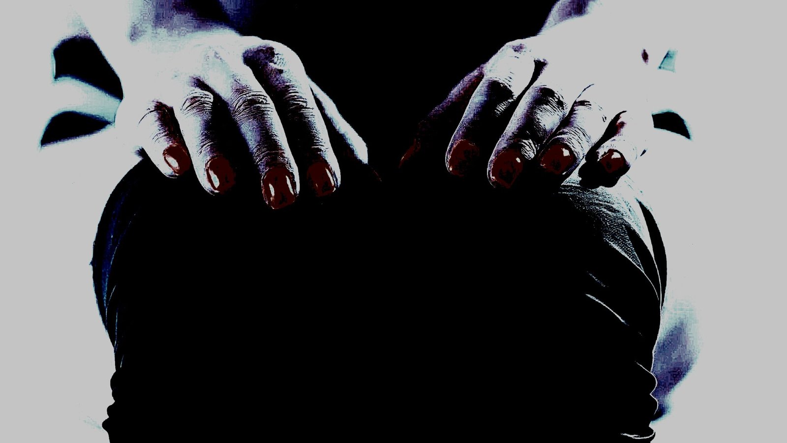 Close-up of hands with red nails resting on black fabric, creating a mysterious and moody feel.