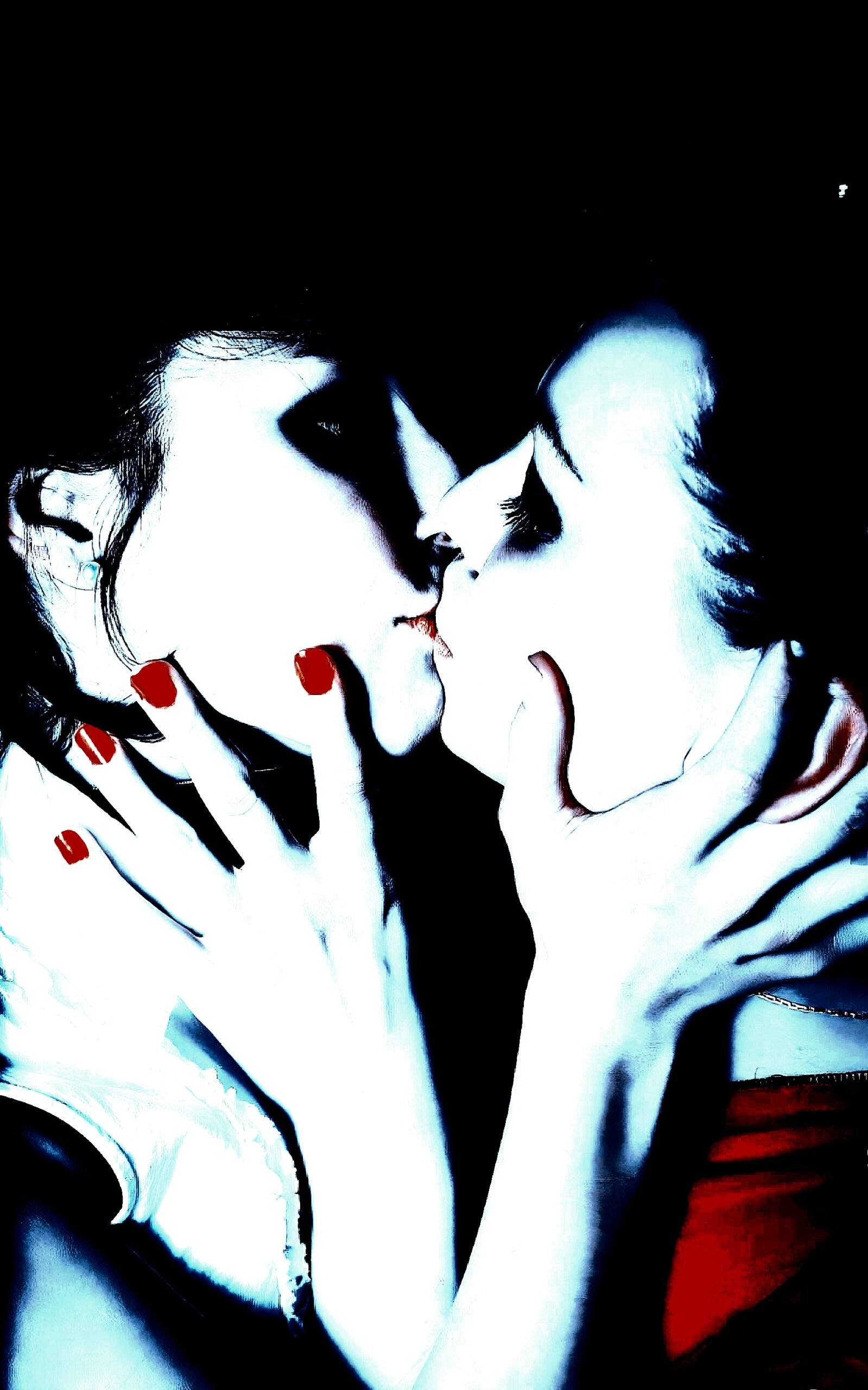Two women sharing an intimate kiss in gothic-style lighting, highlighted with red nail polish and pale tones.