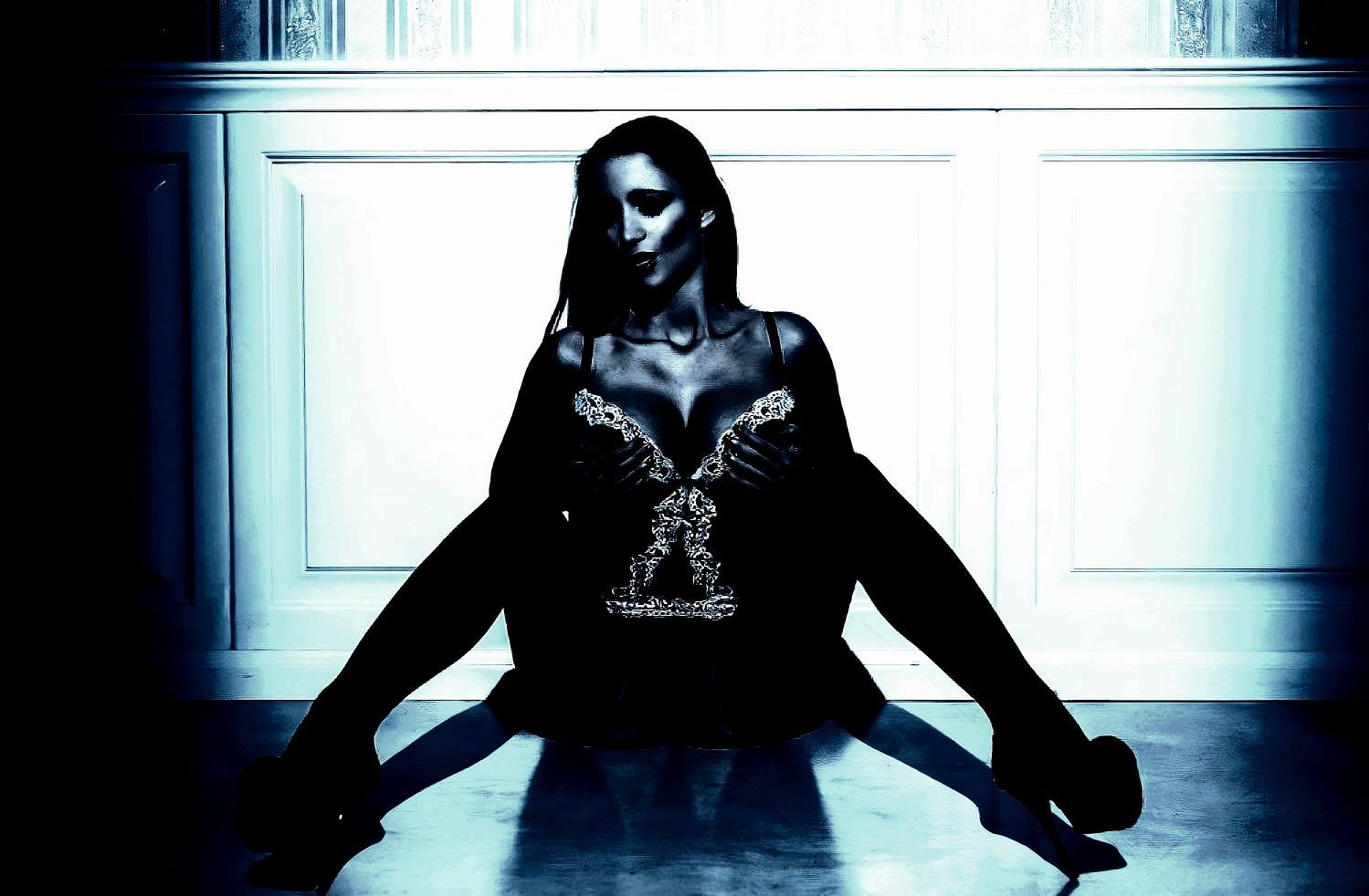 Woman in intricate lingerie sitting on the floor with dramatic lighting, emphasizing her bold and commanding presence.