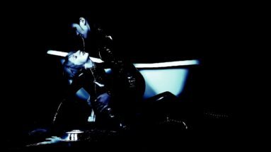 One woman leaning over another in a dark room near a bathtub, evoking a dramatic and intense connection.