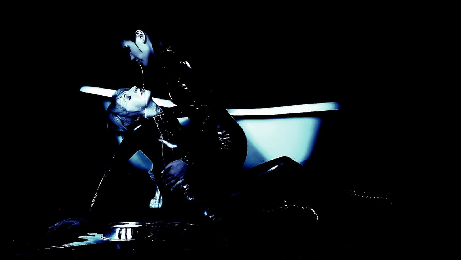 One woman leaning over another in a dark room near a bathtub, evoking a dramatic and intense connection.