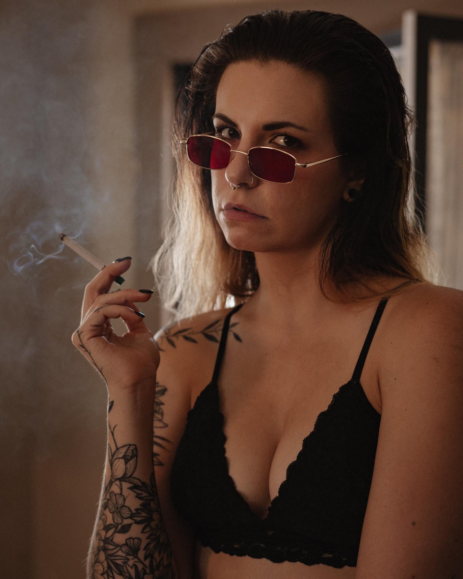 Woman with red sunglasses, smoking and staring intensely at the camera, exuding confidence and edge.