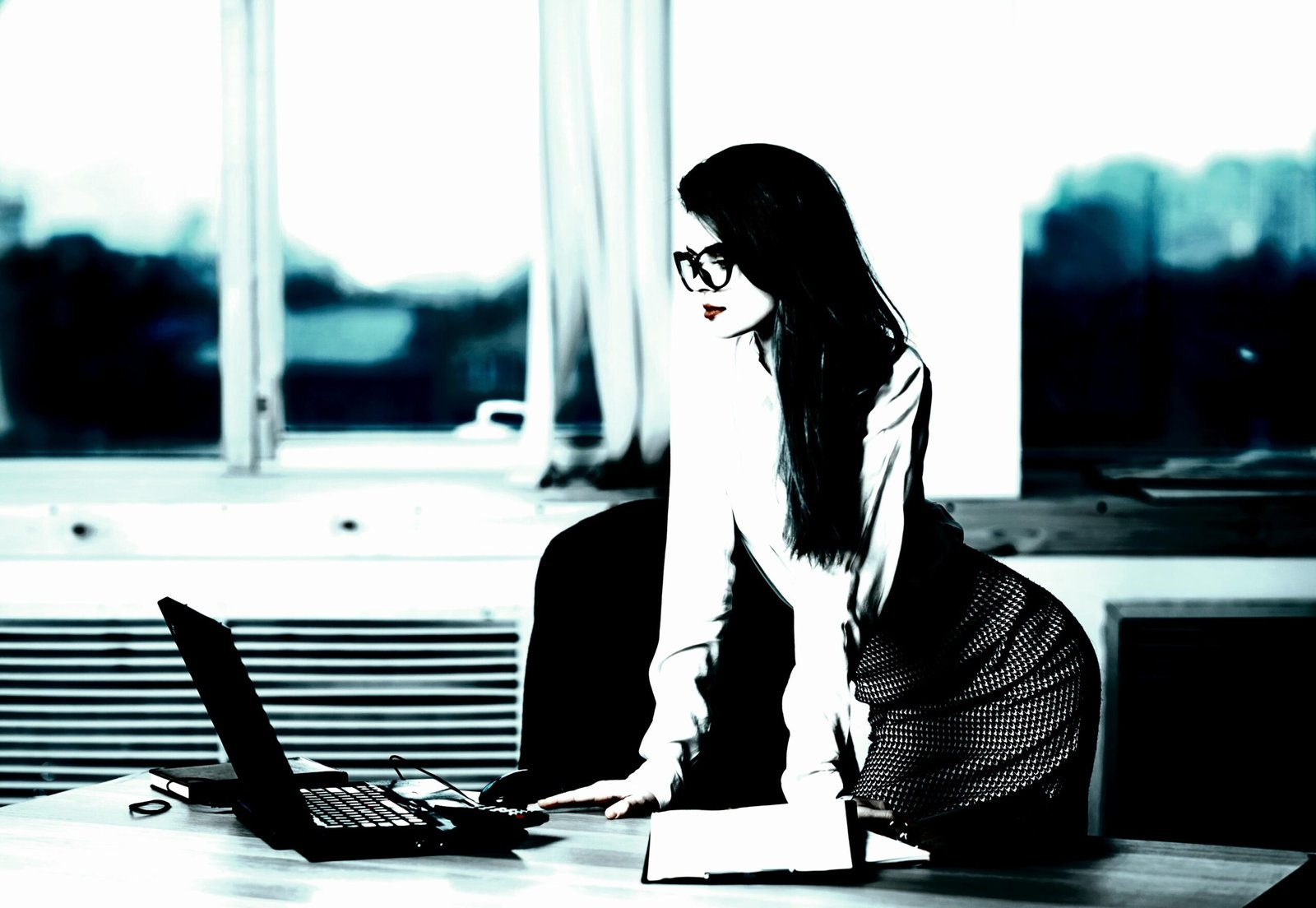 Focused businesswoman leaning over a desk with a laptop, showcasing a determined and poised demeanor.