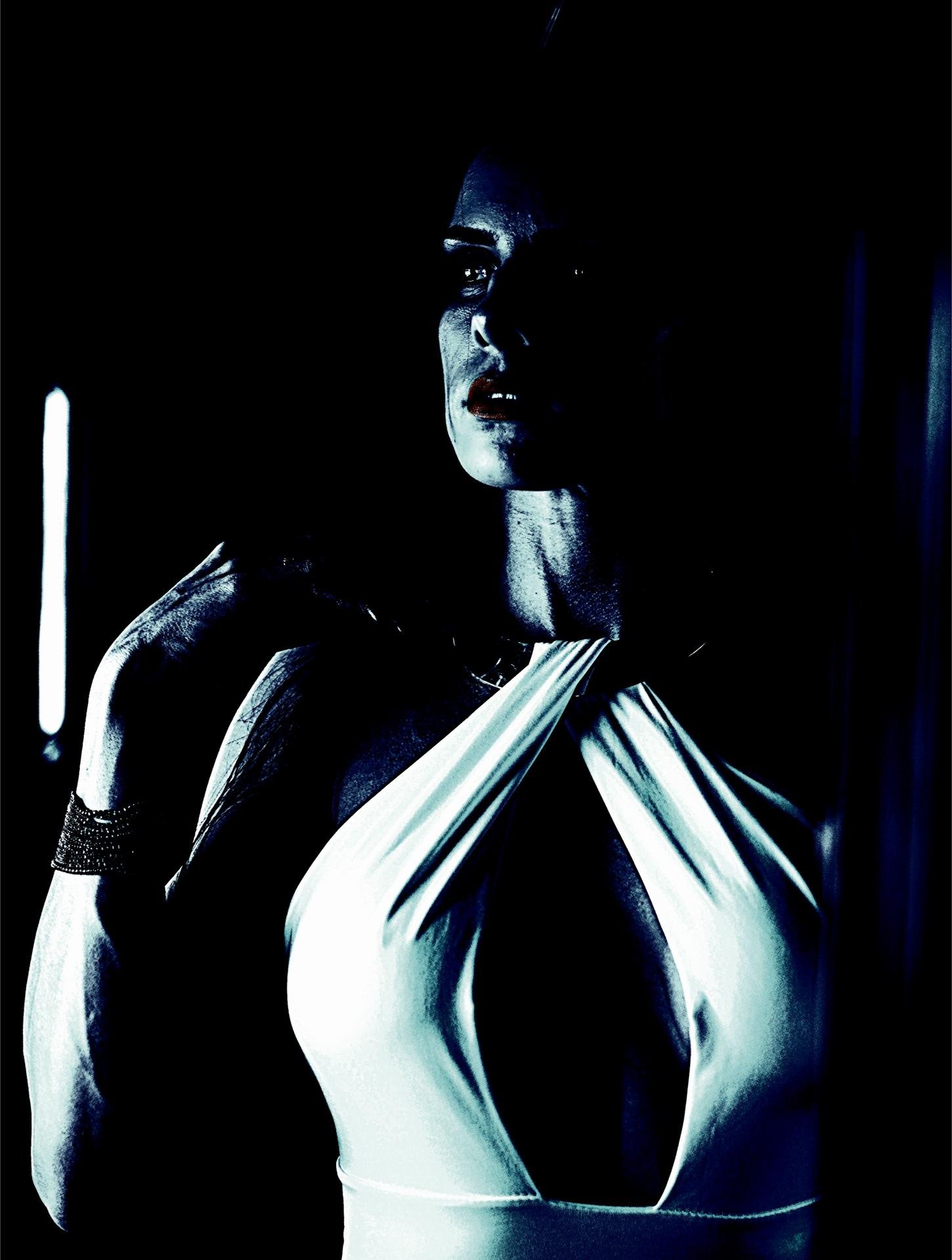 A woman in a dramatic white halter-neck gown, partially illuminated in a moody, gothic setting.