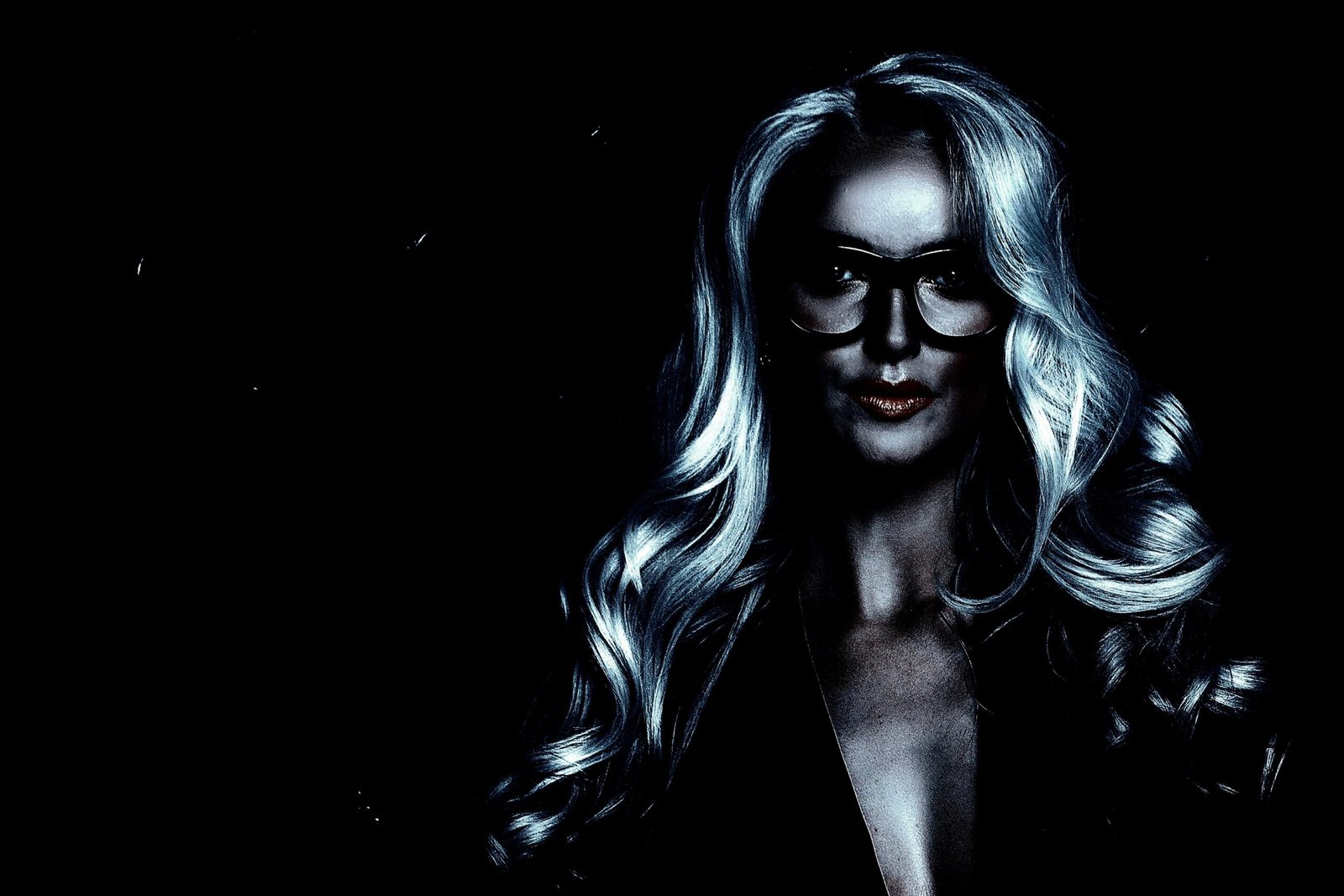 Close-up portrait of a glamorous woman with wavy silver hair and bold glasses, illuminated dramatically.