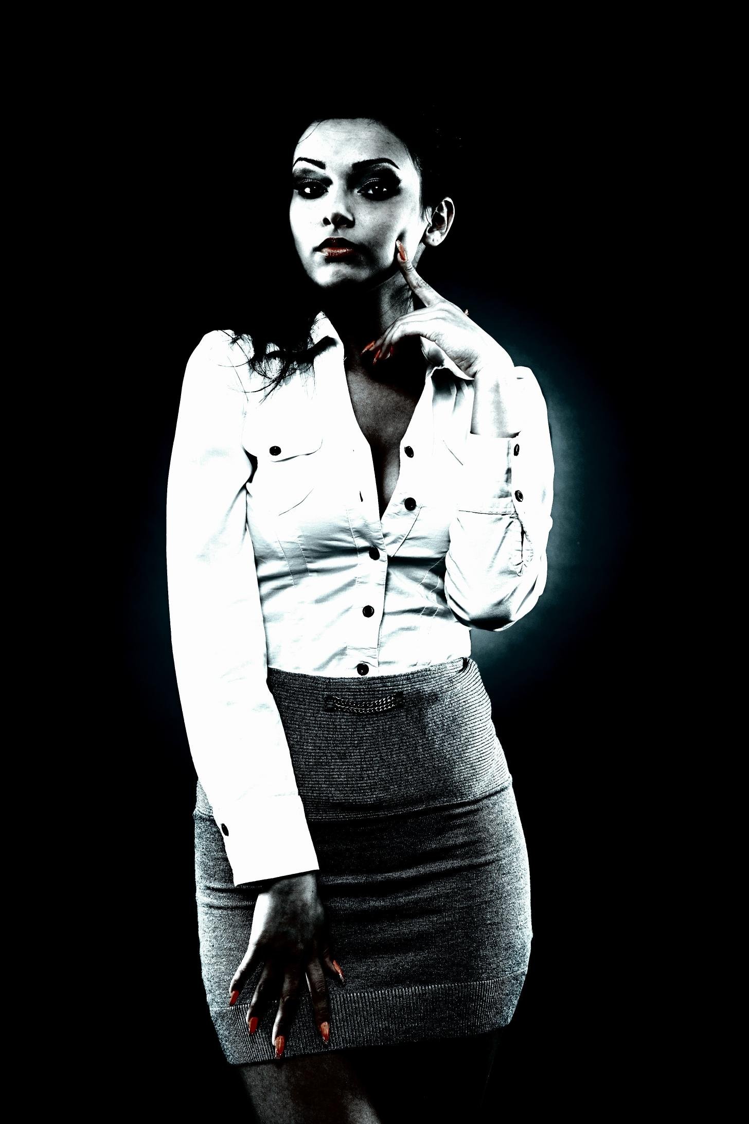 Woman in a fitted white blouse and gray skirt, standing confidently with a thoughtful pose, set against a dark background.