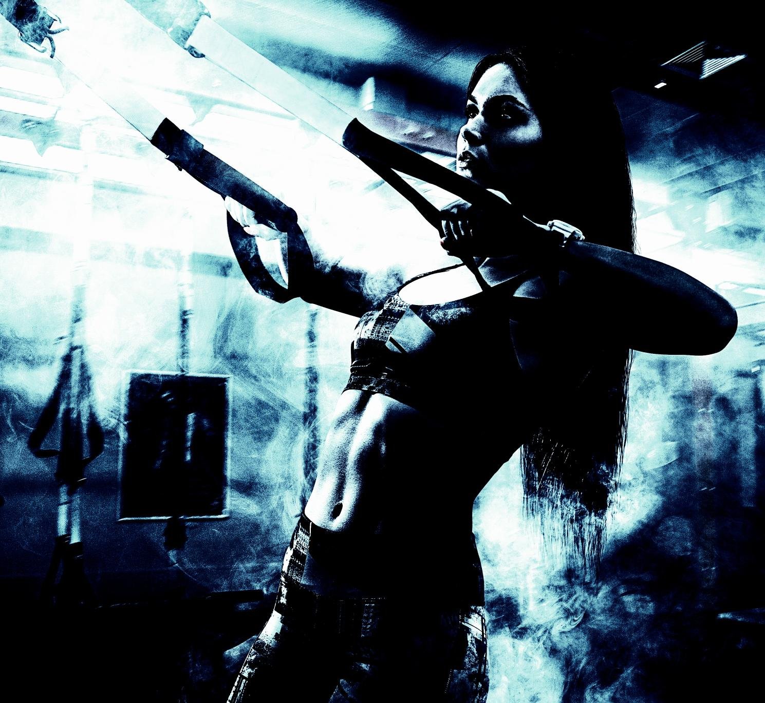 Alternative athlete using suspension straps in a dimly lit, gritty gym with a smoky background.