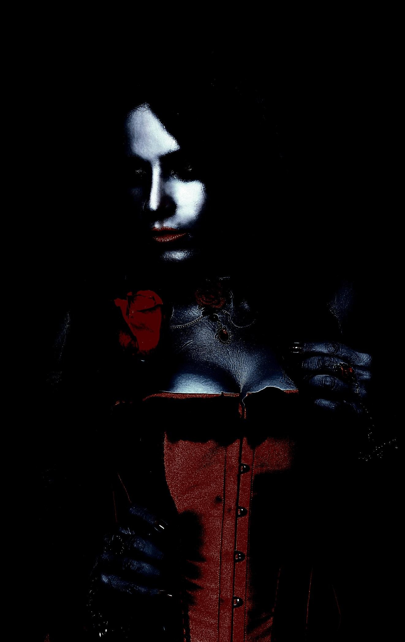 Moody portrait of a woman in a red gothic corset adorned with a rose, her face partially illuminated against a dark background.