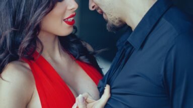 Woman in a red dress looking upwards passionately, her hand pulling on her partner’s shirt.