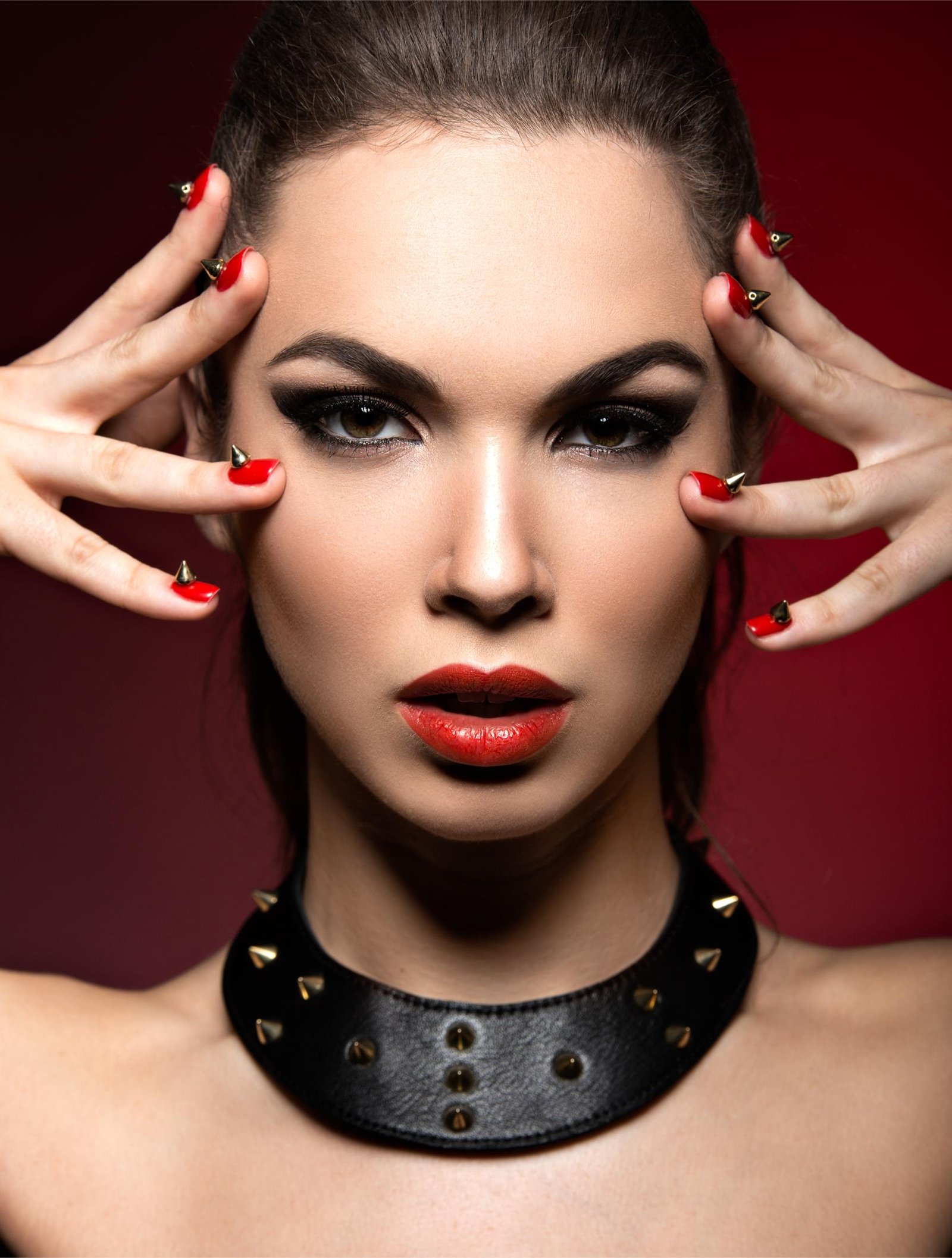 A striking woman wearing a studded leather choker with bold red lipstick and spiked nail designs, embodying edgy gothic fashion.