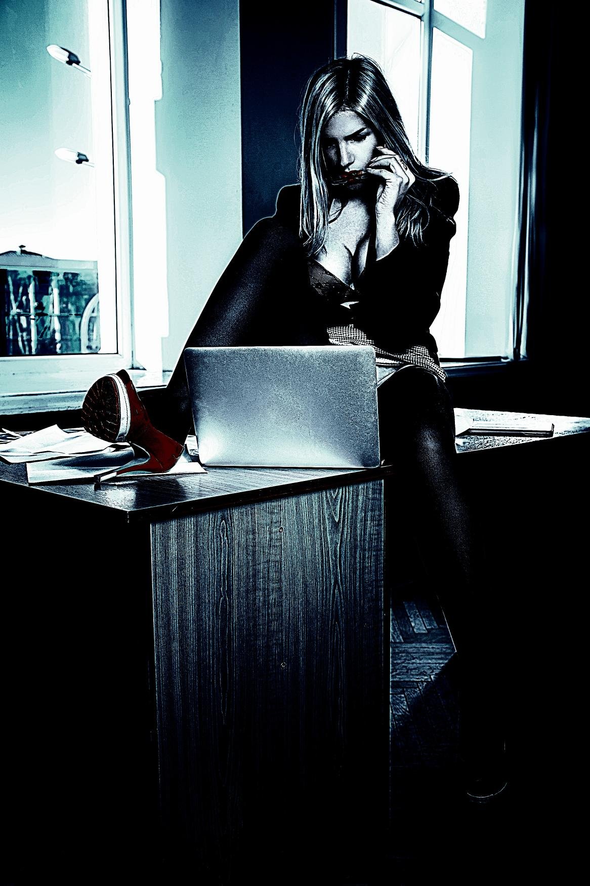 Confident businesswoman sitting on a desk with a laptop, dressed in a sleek outfit and high heels.