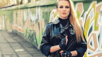 Woman in a black leather jacket with gloves, standing in front of a graffiti wall, embodying urban metal style.