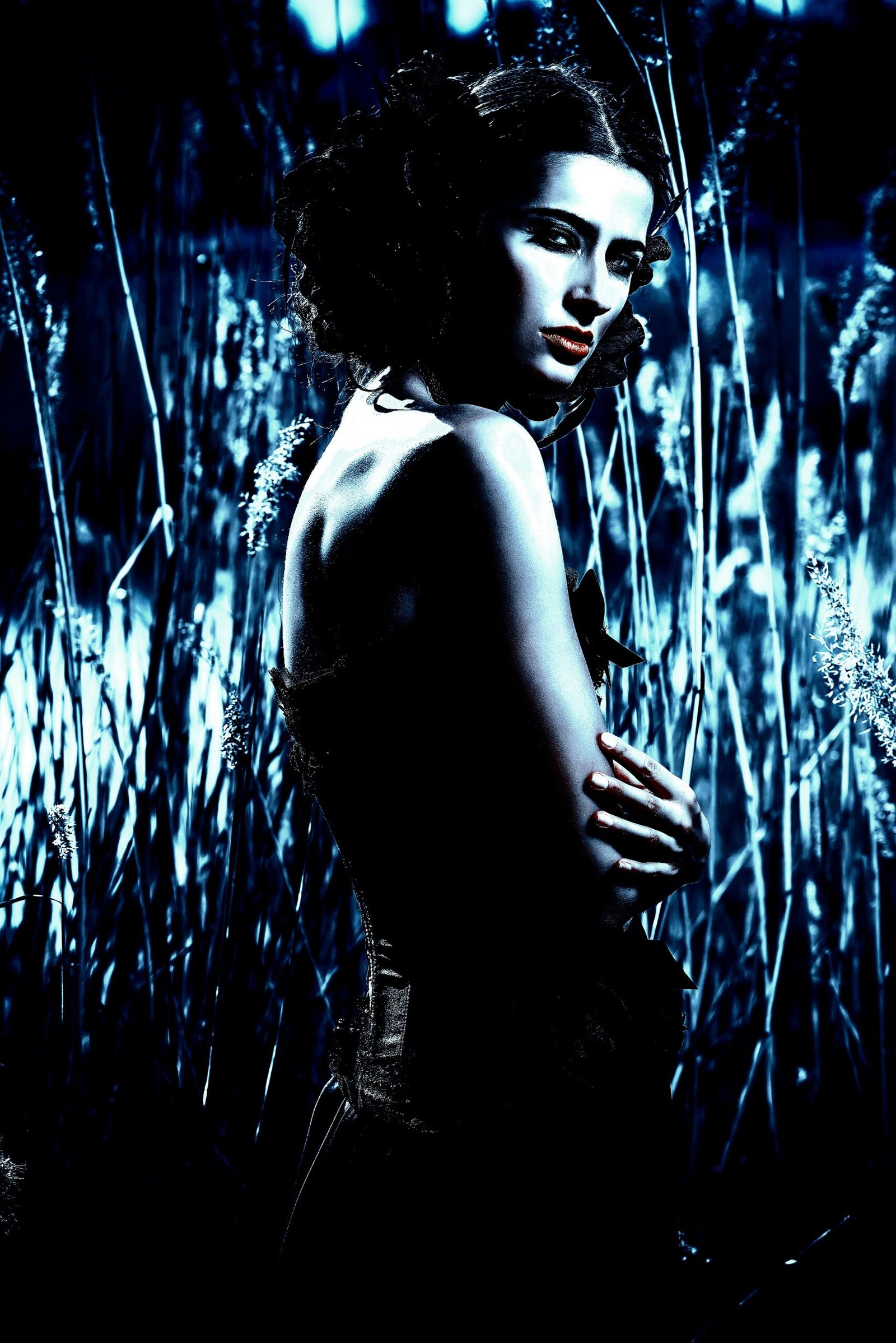 Gothic woman in a long black gown reclining on a fallen tree in a dark, eerie forest setting. 