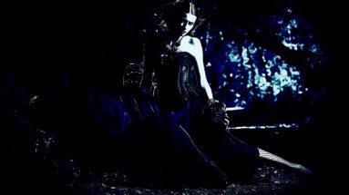Gothic woman with a somber expression, standing in a field of tall grass, dressed in a dark, elegant gown.