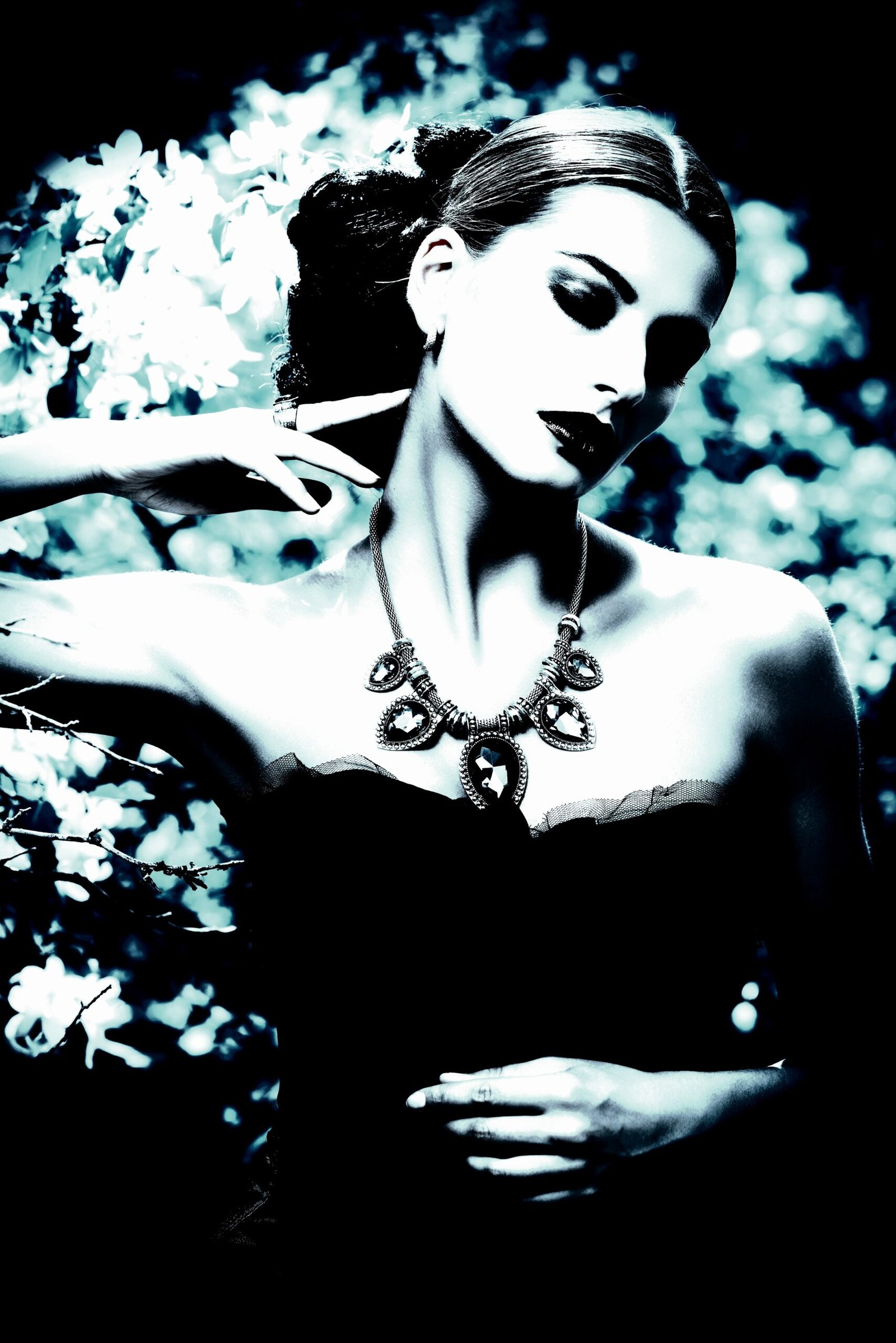 Close-up of a gothic woman with dark makeup, striking jewelry, and an intense expression against a moody background.