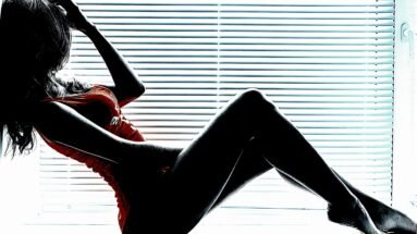 Silhouette of a woman sitting by a window with blinds, highlighting an artistic and moody atmosphere.