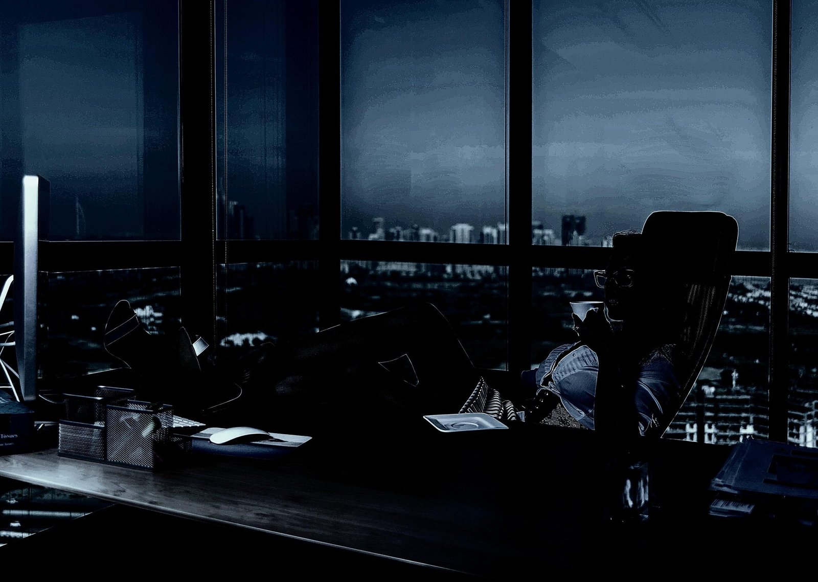 Executive relaxing in a high-rise office at night, surrounded by city lights and a luxurious workspace.