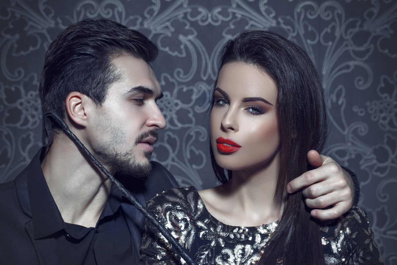 Man holding a leather whip near a woman's neck, capturing a subtle exchange of power and control.