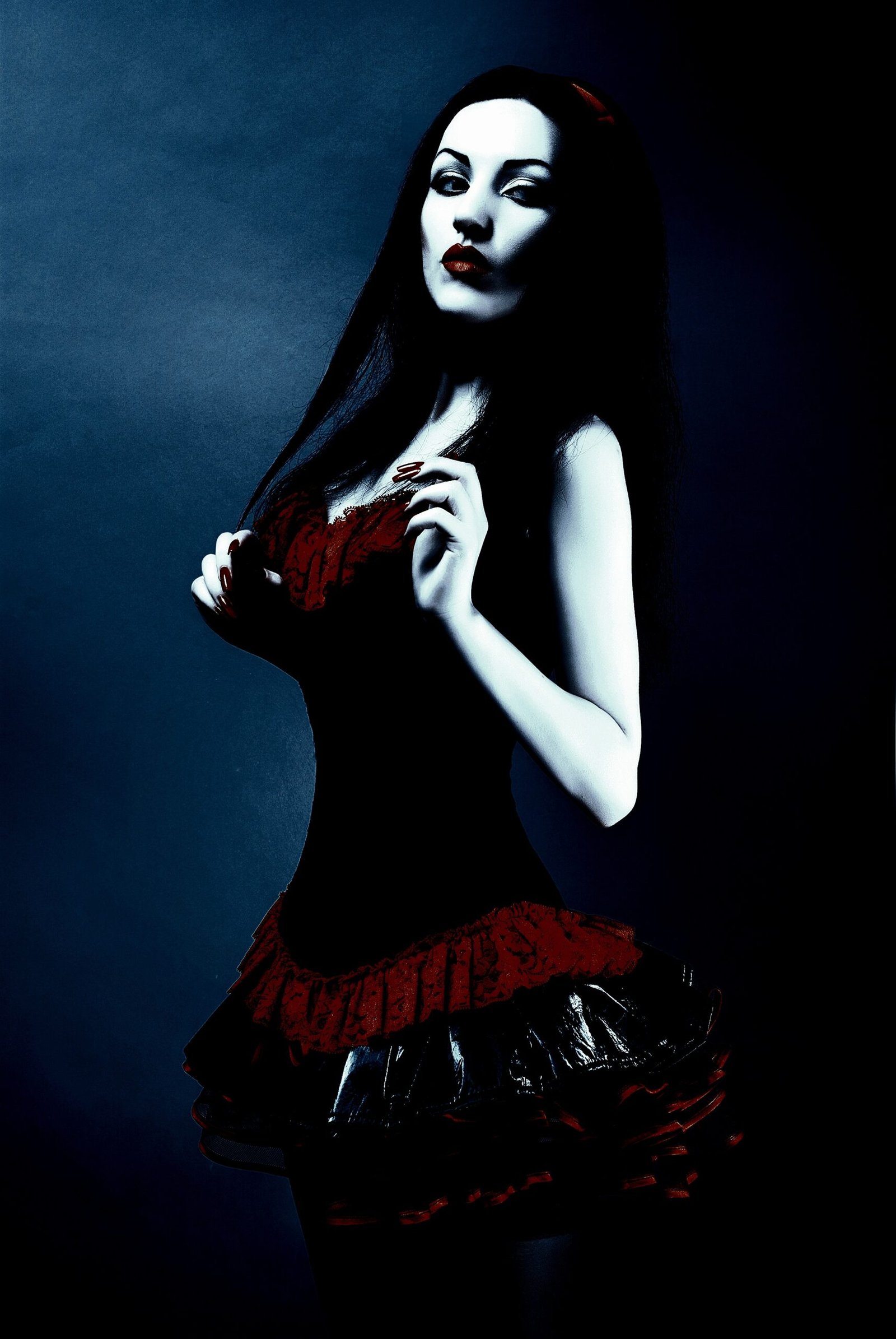 A person with long dark hair wearing a black and red corset dress with a ruffled skirt. The person's face is blurred.
